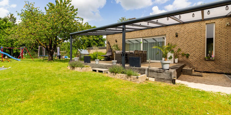 Weitläufiger Garten mit gepflegtem Rasen, Spielbereich und hochwertiger Terrassenüberdachung.